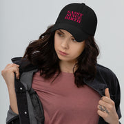 Black low-profile dad cap worn by a woman, embroidered in pink with the words Sassy Since Birth.