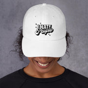 White low-profile dad cap worn by a woman, embroidered in black with the words I Hate People.