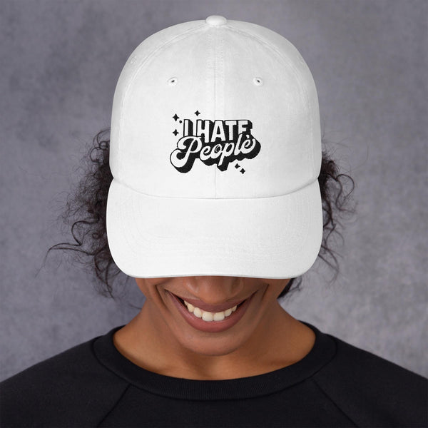 White low-profile dad cap worn by a woman, embroidered in black with the words I Hate People.