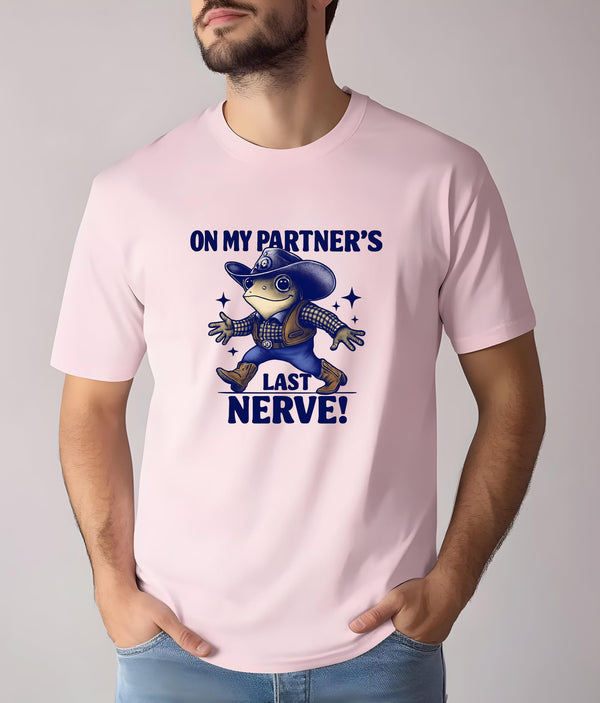 May include: Pale pink t-shirt with a cartoon frog in a cowboy outfit. The frog is wearing a blue hat, vest, and boots. The text "ON MY PARTNER'S LAST NERVE!" is printed in navy blue. The design includes star accents.