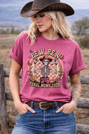 Western graphic t-shirt with skeleton cowgirl holding guns, “Pew Pew Feral Moms Club” text, and vintage floral design, worn in a country-style outdoor setting.