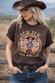 Western graphic t-shirt with skeleton cowgirl holding guns, “Pew Pew Feral Moms Club” text, and vintage floral design, worn in a country-style outdoor setting.