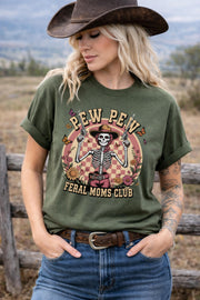 Western graphic t-shirt with skeleton cowgirl holding guns, “Pew Pew Feral Moms Club” text, and vintage floral design, worn in a country-style outdoor setting.