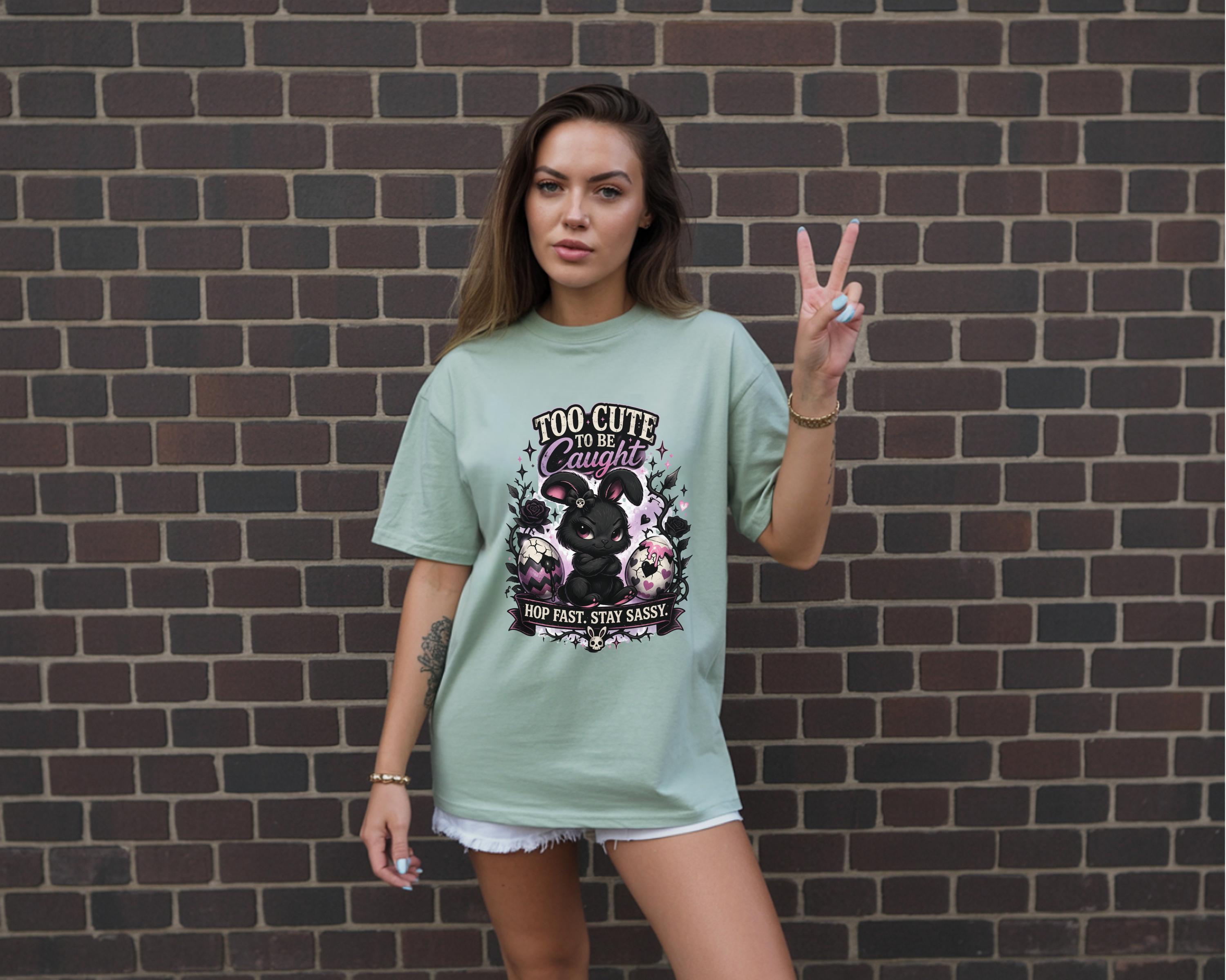 Woman wearing black graphic t-shirt with cute edgy bunny illustration and text Too Cute To Be Caught styled with denim shorts and accessories