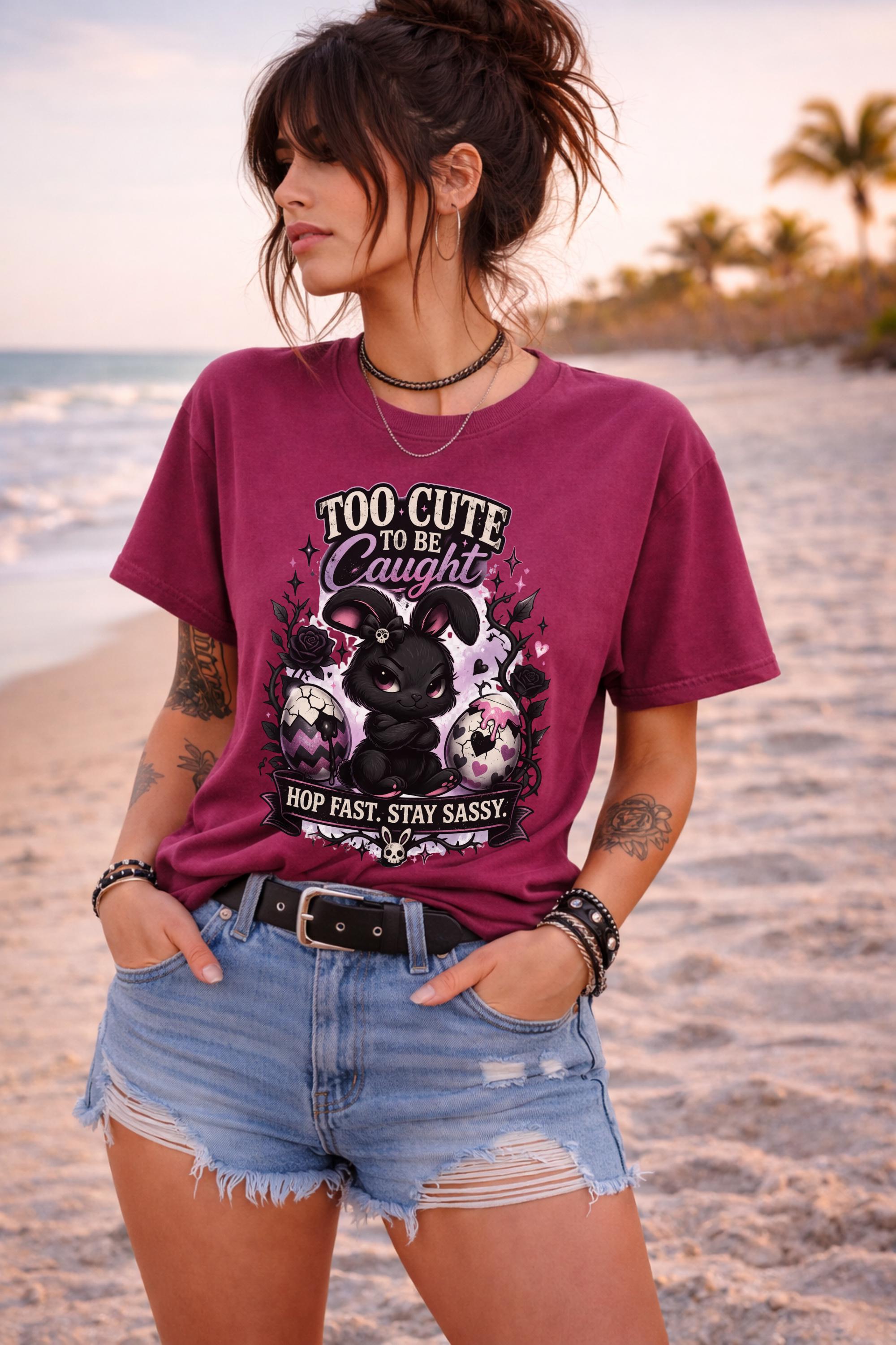 Woman wearing black graphic t-shirt with cute edgy bunny illustration and text Too Cute To Be Caught styled with denim shorts and accessories