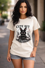 Graphic t-shirt featuring gothic bunny with glowing eyes and “Cute But Psycho” text, worn by model on beach with casual summer outfit