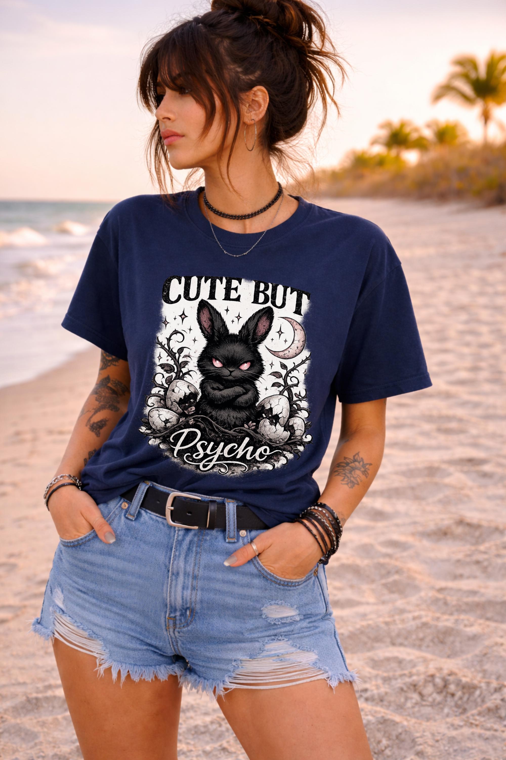 Graphic t-shirt featuring gothic bunny with glowing eyes and “Cute But Psycho” text, worn by model on beach with casual summer outfit