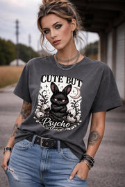 Graphic t-shirt featuring gothic bunny with glowing eyes and “Cute But Psycho” text, worn by model on beach with casual summer outfit