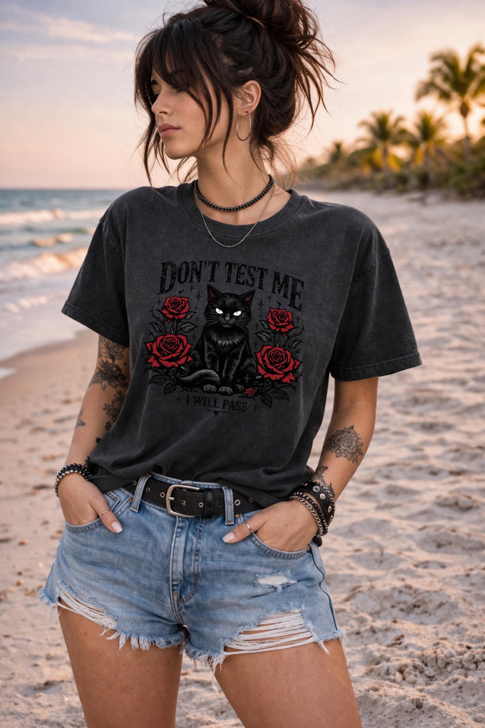 Graphic t-shirt featuring black cat with red roses and “Don’t Test Me I Will Pass” text, styled on model with edgy casual outfit in urban setting