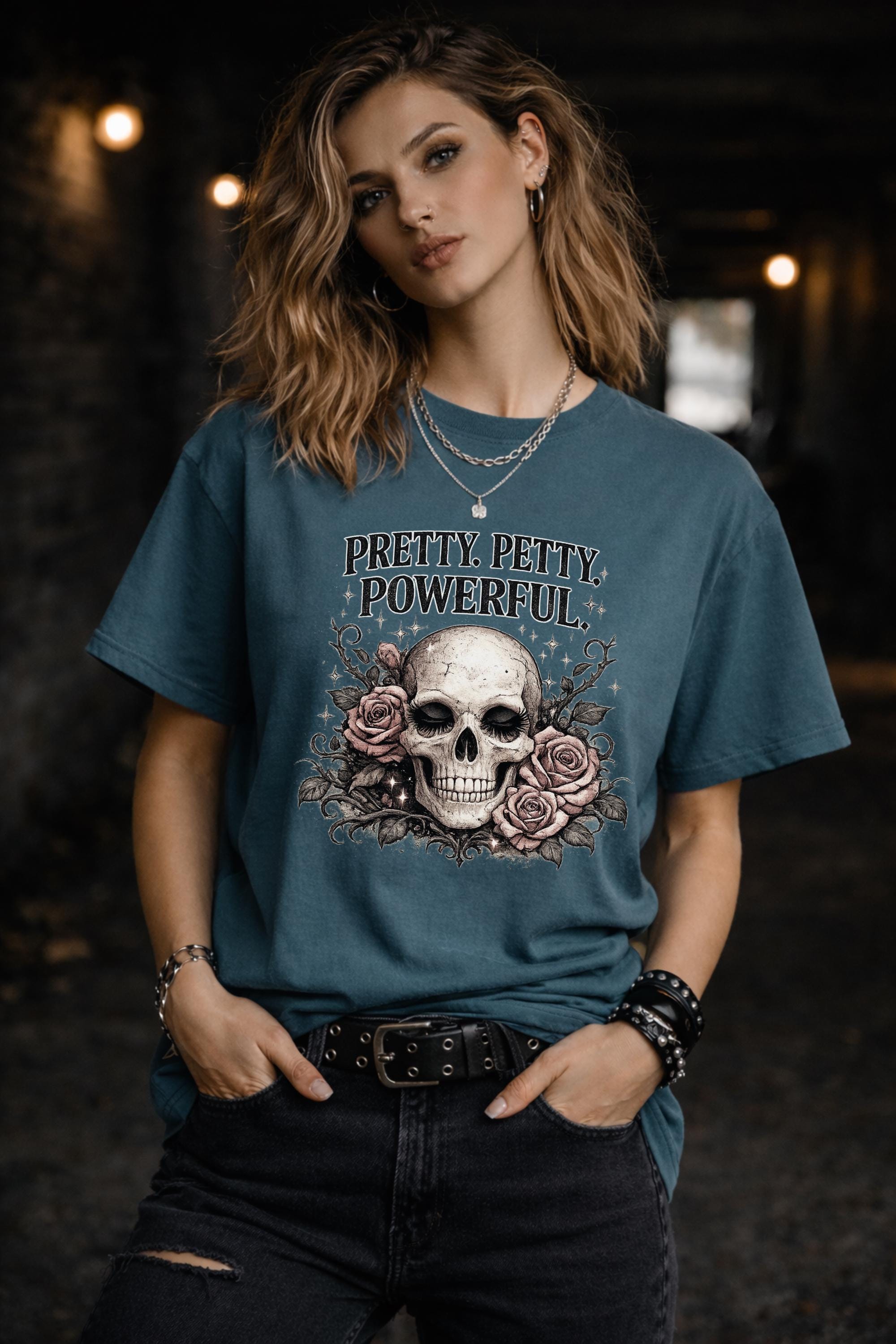 Graphic t-shirt featuring skull with roses and “Pretty Petty Powerful” text, styled on model with edgy streetwear aesthetic and dark neutral backdrop