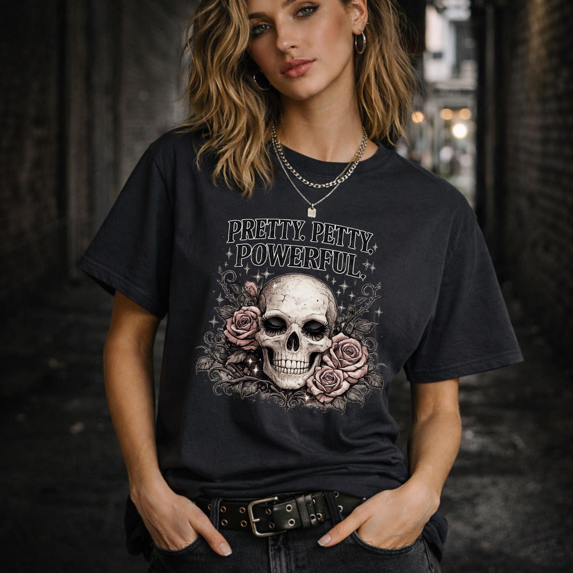 Graphic t-shirt featuring skull with roses and “Pretty Petty Powerful” text, styled on model with edgy streetwear aesthetic and dark neutral backdrop