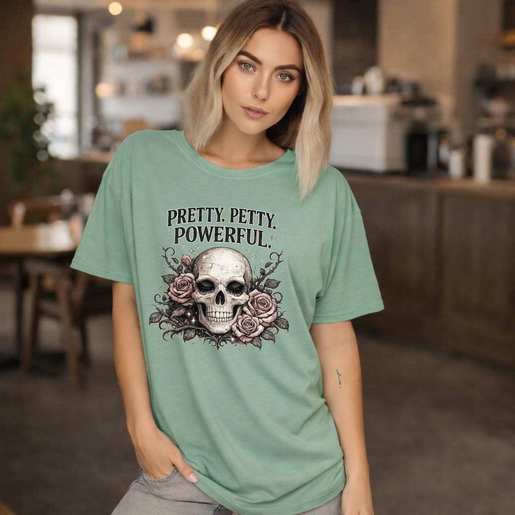 Graphic t-shirt featuring skull with roses and “Pretty Petty Powerful” text, styled on model with edgy streetwear aesthetic and dark neutral backdrop
