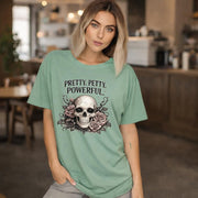 Graphic t-shirt featuring skull with roses and “Pretty Petty Powerful” text, styled on model with edgy streetwear aesthetic and dark neutral backdrop