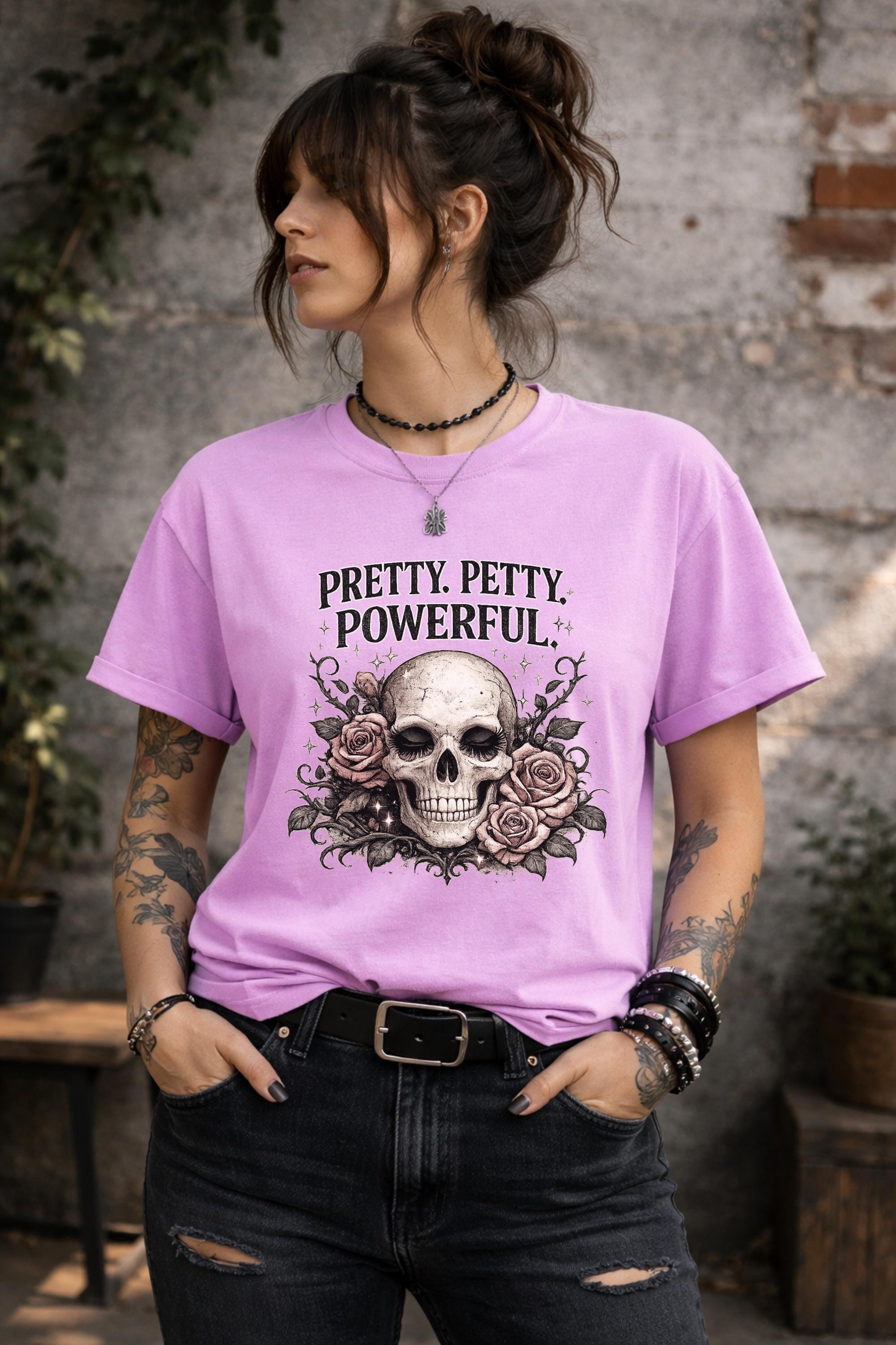 Graphic t-shirt featuring skull with roses and “Pretty Petty Powerful” text, styled on model with edgy streetwear aesthetic and dark neutral backdrop