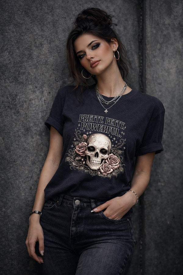 Graphic t-shirt featuring skull with roses and “Pretty Petty Powerful” text, styled on model with edgy streetwear aesthetic and dark neutral backdrop