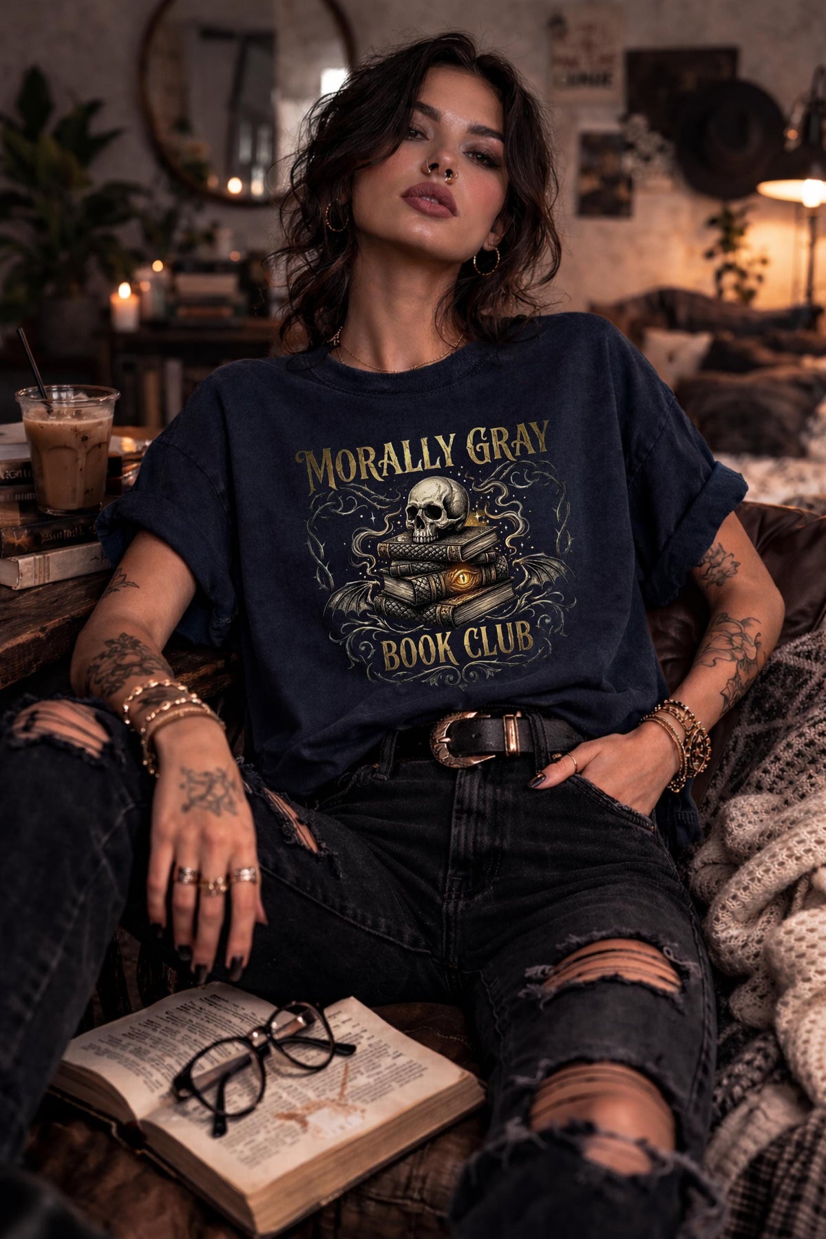 Woman wearing a true navy “Morally Gray Book Club” graphic t-shirt featuring a skull on stacked books with a glowing eye, styled in a dark academia aesthetic against a moody textured background.