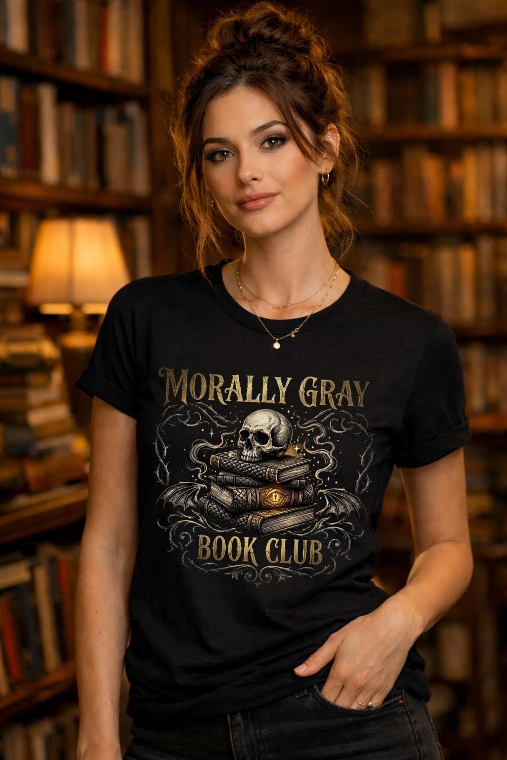 Woman wearing a black “Morally Gray Book Club” graphic t-shirt featuring a skull on stacked books with a glowing eye, styled in a dark academia aesthetic against a moody textured background.