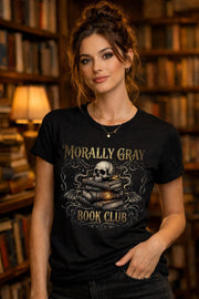 Woman wearing a black “Morally Gray Book Club” graphic t-shirt featuring a skull on stacked books with a glowing eye, styled in a dark academia aesthetic against a moody textured background.
