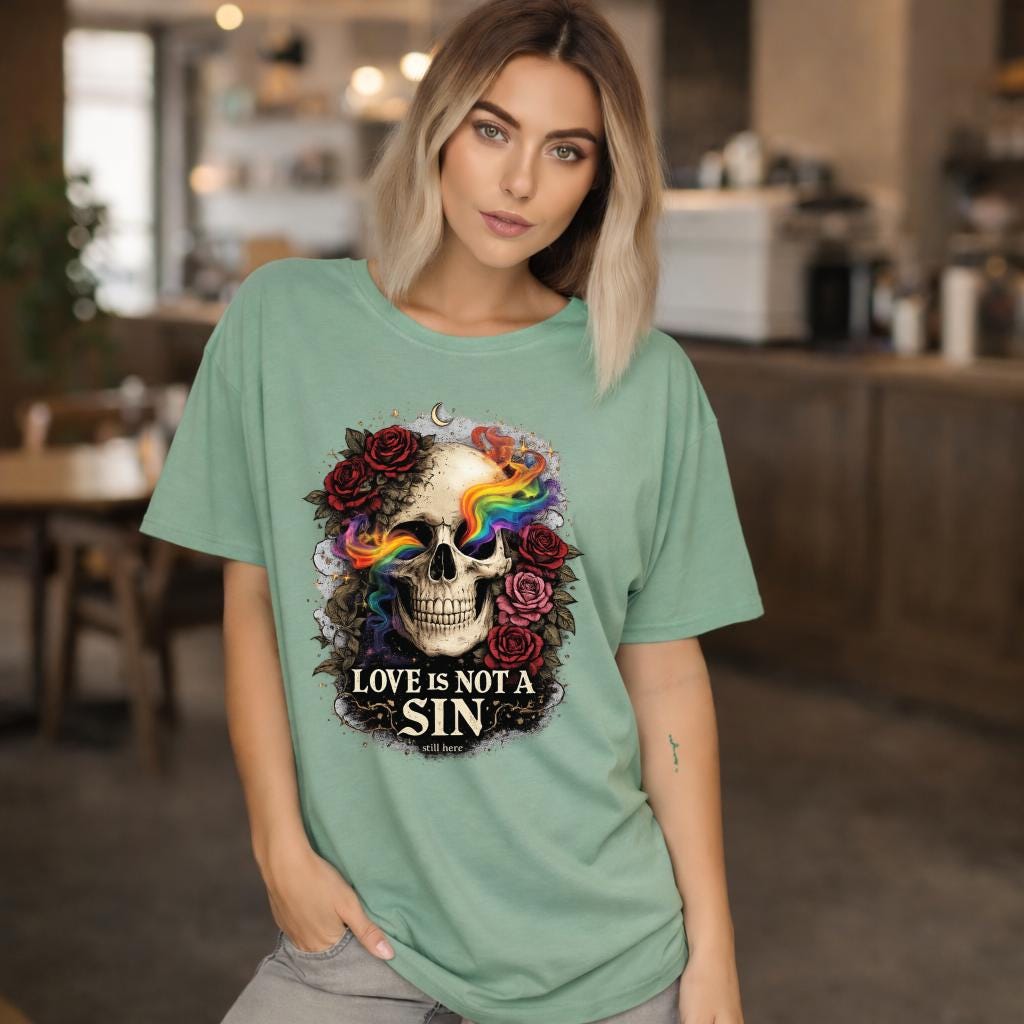 Graphic t-shirt featuring skull with rainbow accents and roses with “Love Is Not a Sin” text, styled on model with edgy alternative streetwear aesthetic