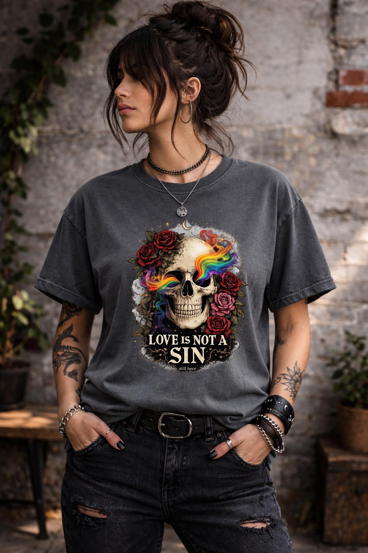 Dark gray graphic t-shirt featuring skull with rainbow accents and roses with “Love Is Not a Sin” text, styled on model with edgy alternative streetwear aesthetic