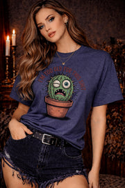 Woman wearing a  Gildan 5000 t-shirt featuring a funny cactus graphic with the phrase “I’m too old for this shit,” styled with black distressed shorts in a warm, dark aesthetic setting.
