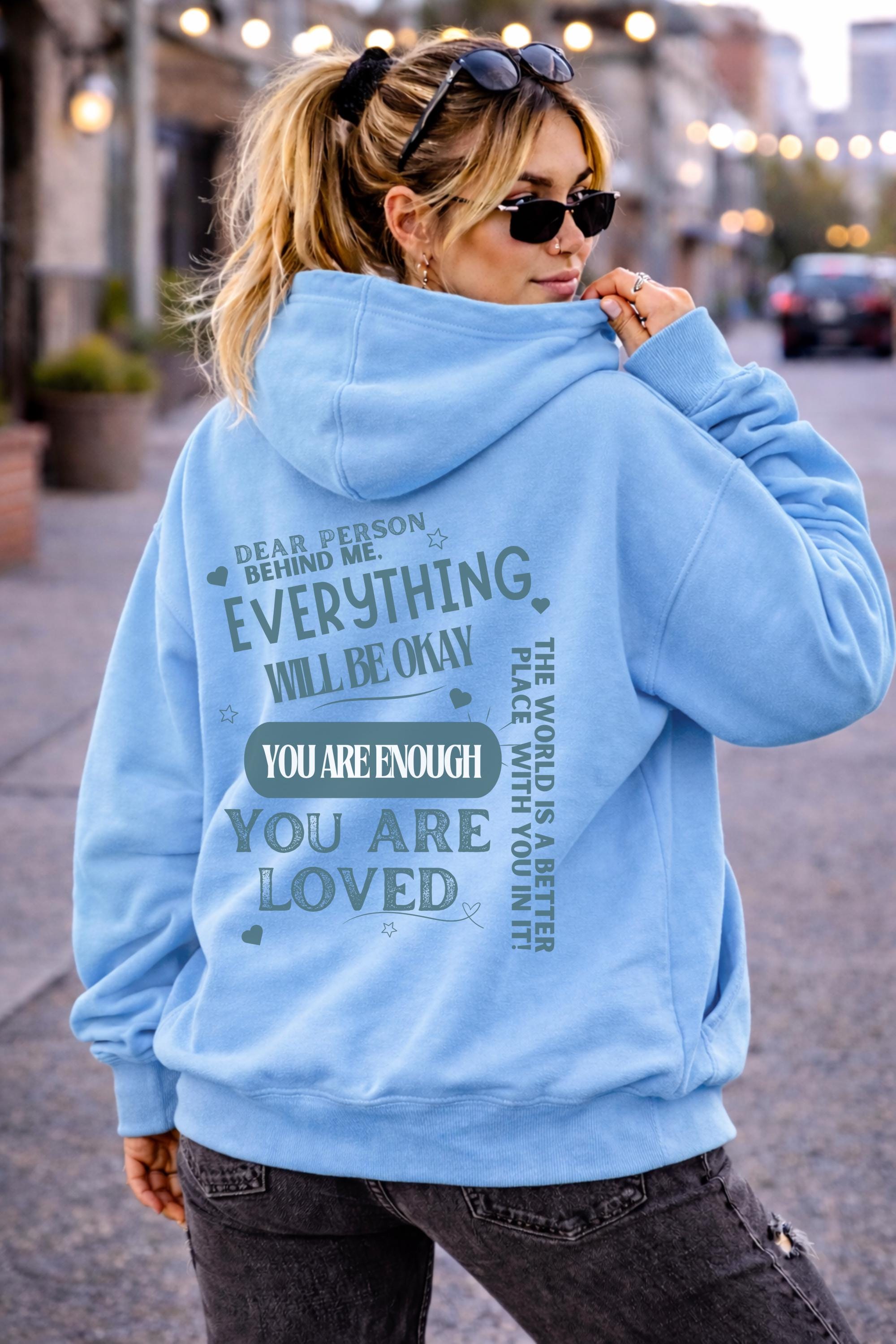 Woman wearing motivational hoodie featuring “you are enough” and “you are loved” message on the back