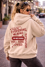 Woman wearing motivational hoodie featuring “you are enough” and “you are loved” message on the back