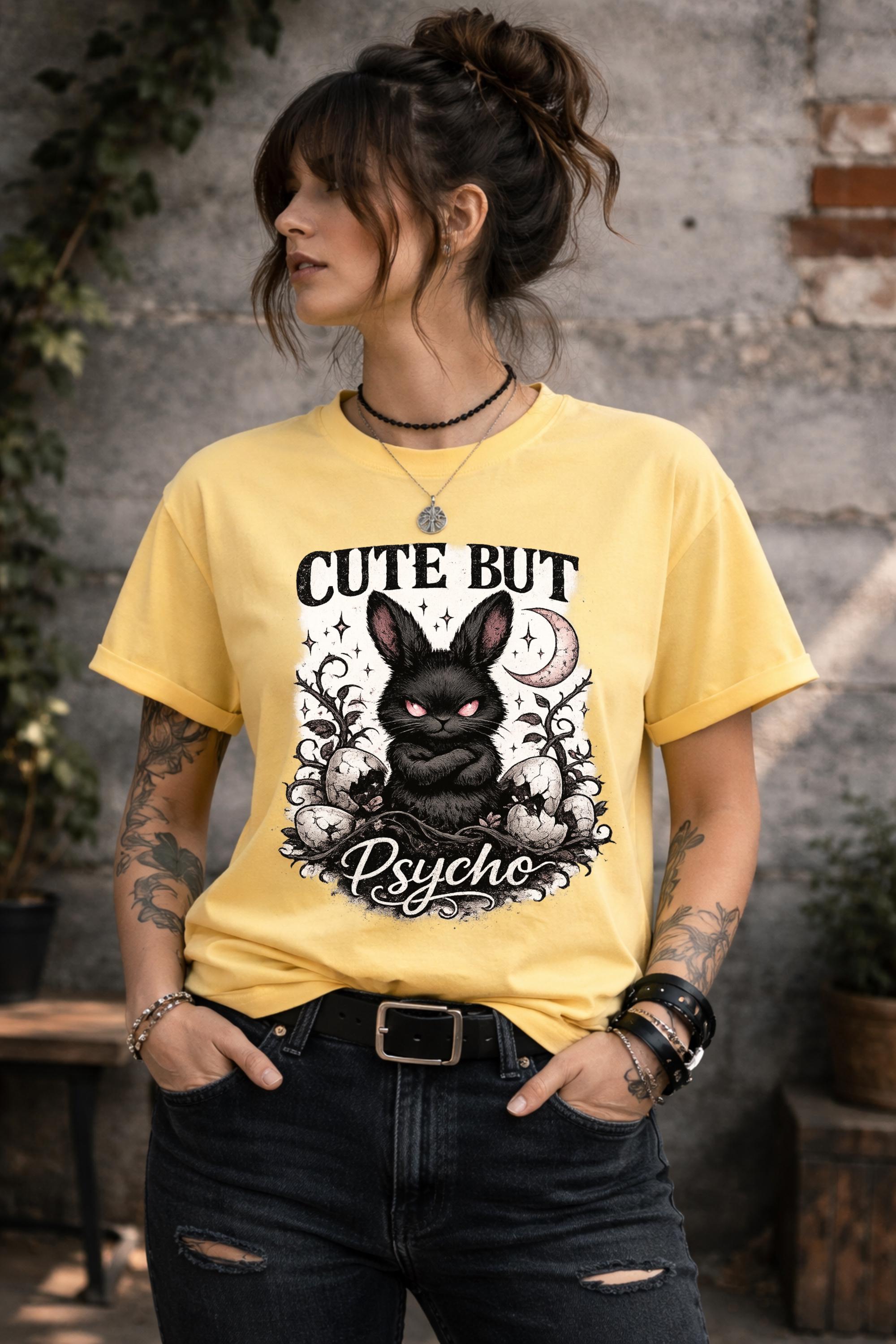 Graphic t-shirt featuring gothic bunny with glowing eyes and “Cute But Psycho” text, worn by model on beach with casual summer outfit