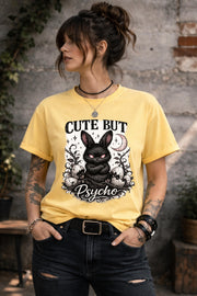 Graphic t-shirt featuring gothic bunny with glowing eyes and “Cute But Psycho” text, worn by model on beach with casual summer outfit