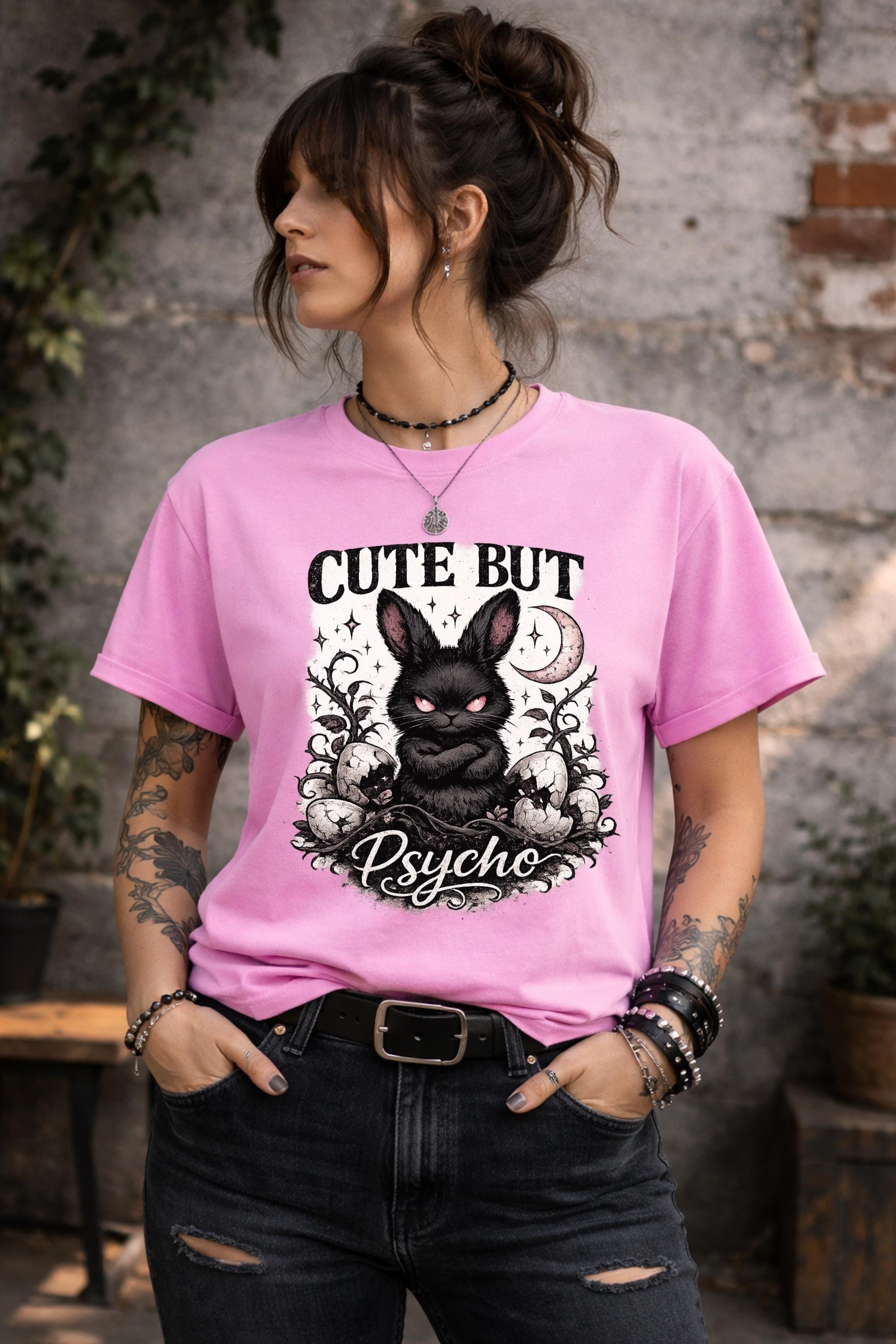 Graphic t-shirt featuring gothic bunny with glowing eyes and “Cute But Psycho” text, worn by model on beach with casual summer outfit