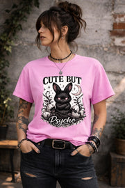 Graphic t-shirt featuring gothic bunny with glowing eyes and “Cute But Psycho” text, worn by model on beach with casual summer outfit