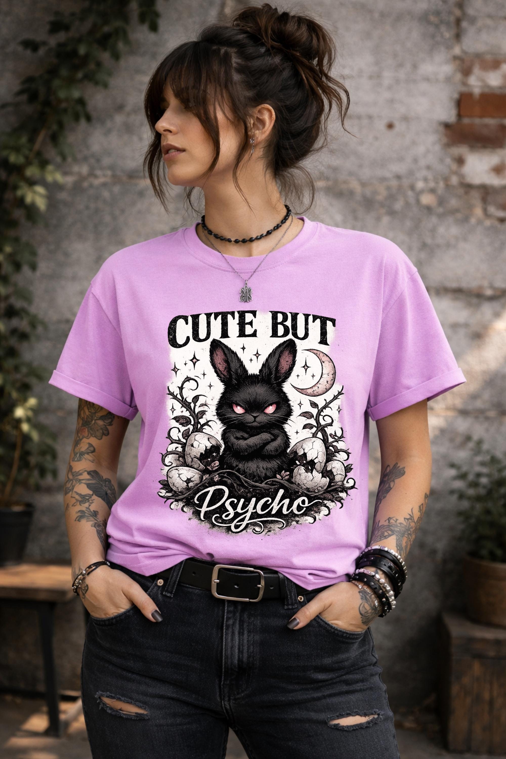 Graphic t-shirt featuring gothic bunny with glowing eyes and “Cute But Psycho” text, worn by model on beach with casual summer outfit