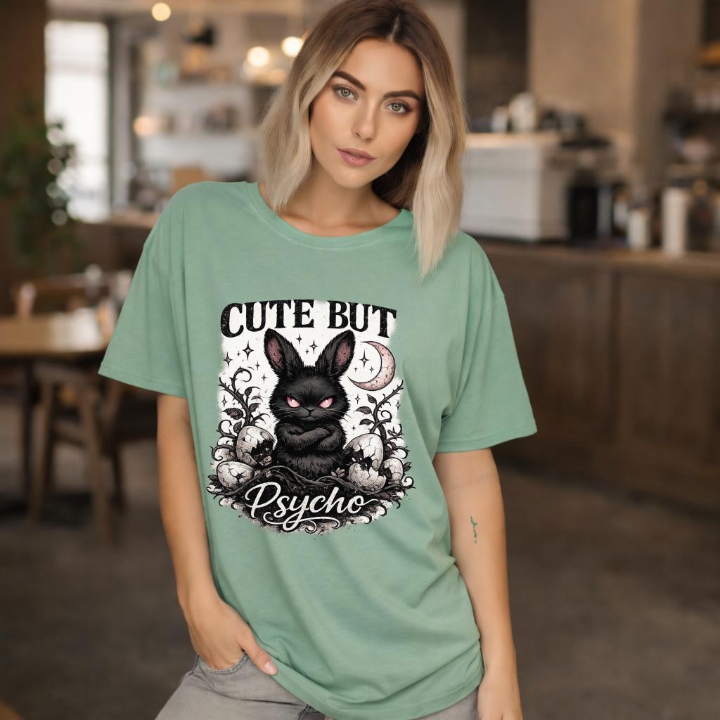 Graphic t-shirt featuring gothic bunny with glowing eyes and “Cute But Psycho” text, worn by model on beach with casual summer outfit