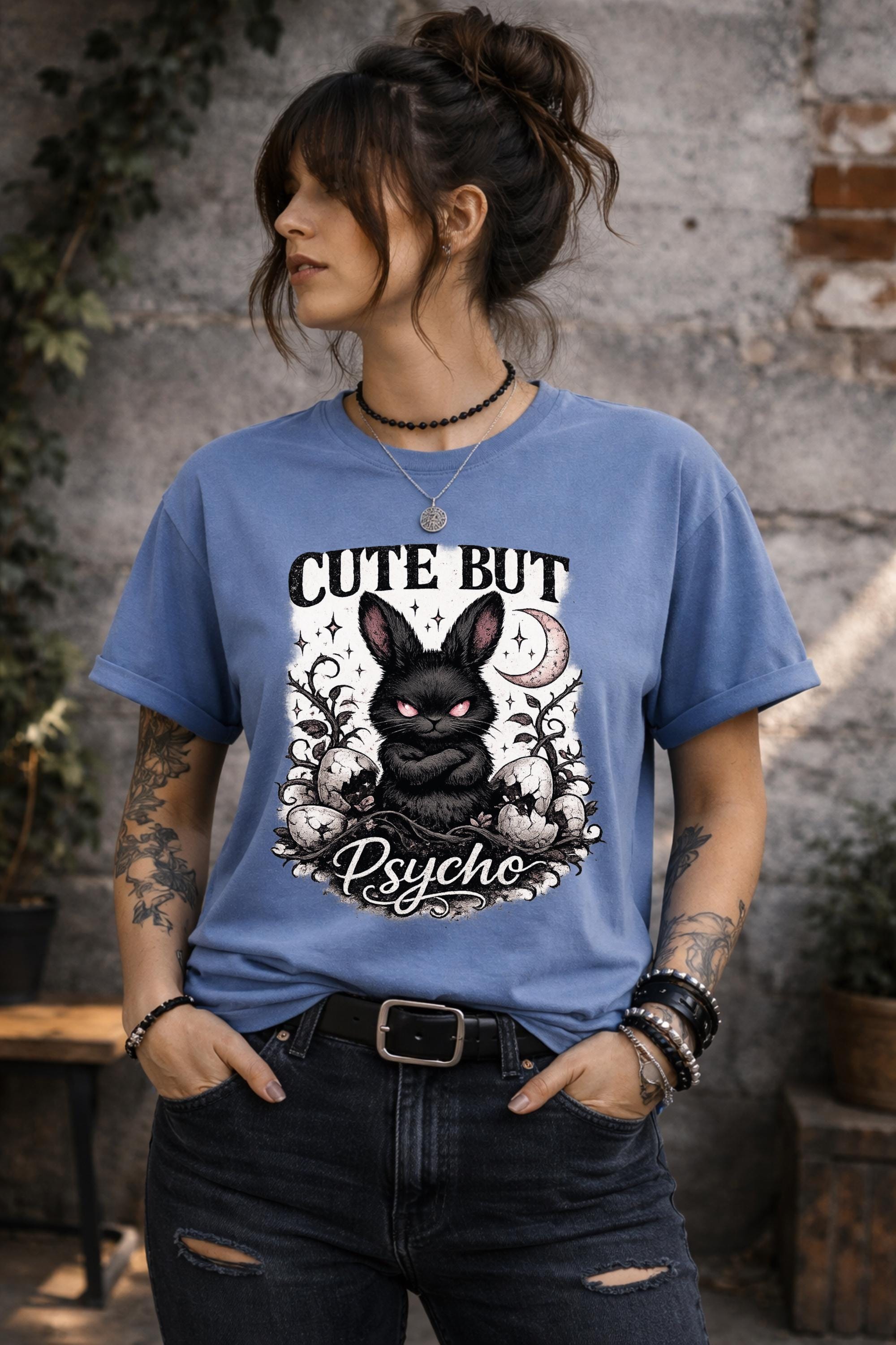 Graphic t-shirt featuring gothic bunny with glowing eyes and “Cute But Psycho” text, worn by model on beach with casual summer outfit
