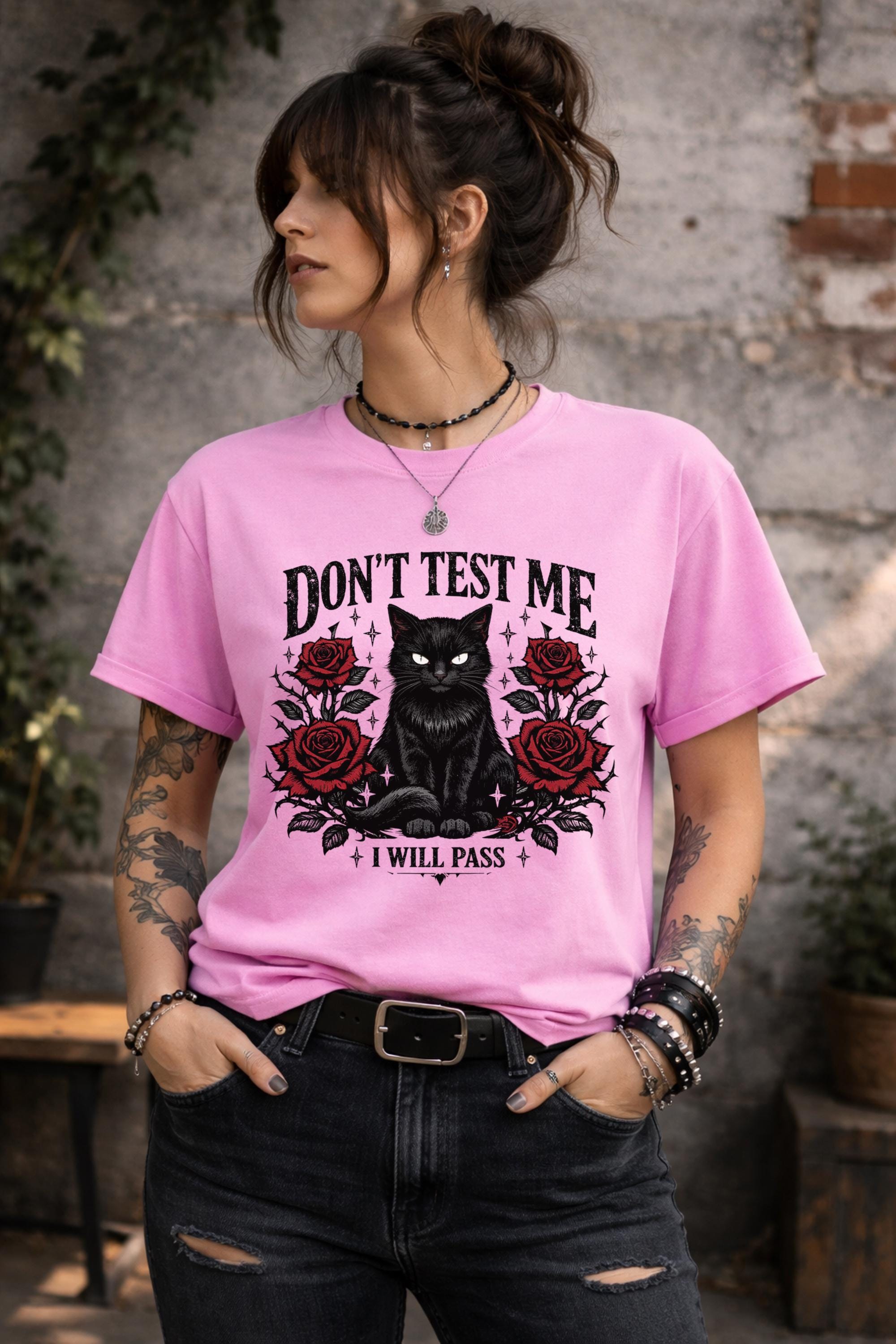Graphic t-shirt featuring black cat with red roses and “Don’t Test Me I Will Pass” text, styled on model with edgy casual outfit in urban setting