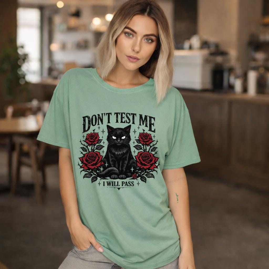 Graphic t-shirt featuring black cat with red roses and “Don’t Test Me I Will Pass” text, styled on model with edgy casual outfit in urban setting