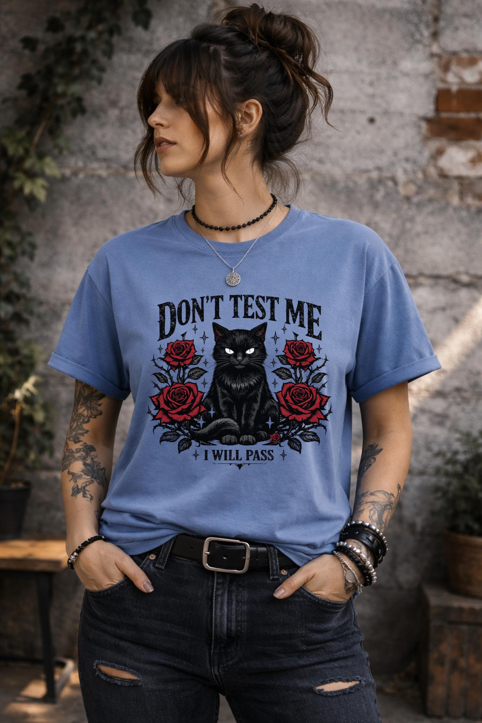 Graphic t-shirt featuring black cat with red roses and “Don’t Test Me I Will Pass” text, styled on model with edgy casual outfit in urban setting