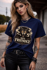 Graphic t-shirt featuring snarling wolf with glowing eyes and “Not Friendly” text, worn by model on beach with casual summer outfit
