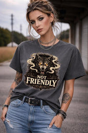 Graphic t-shirt featuring snarling wolf with glowing eyes and “Not Friendly” text, worn by model on beach with casual summer outfit