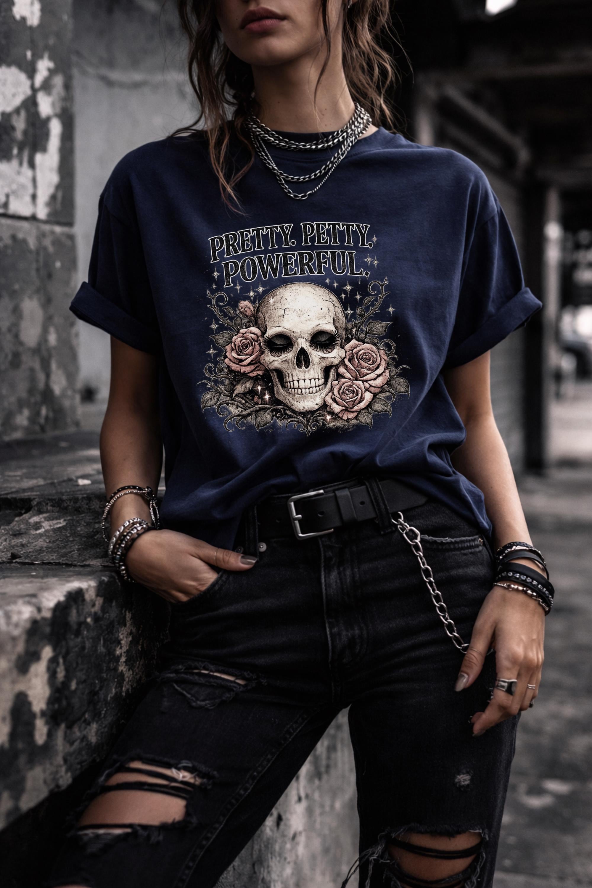 Graphic t-shirt featuring skull with roses and “Pretty Petty Powerful” text, styled on model with edgy streetwear aesthetic and dark neutral backdrop