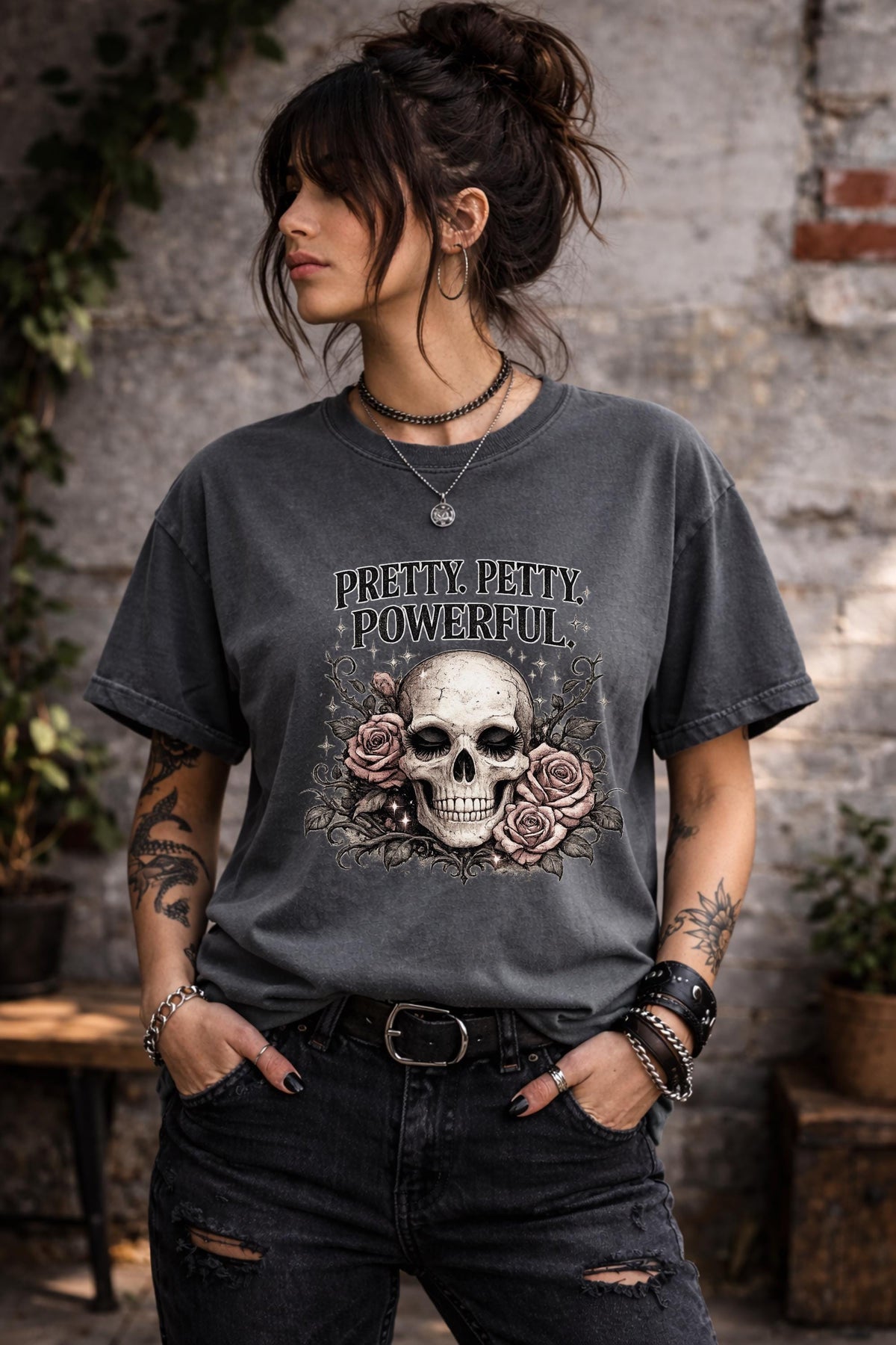 Graphic t-shirt featuring skull with roses and “Pretty Petty Powerful” text, styled on model with edgy streetwear aesthetic and dark neutral backdrop