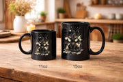 Black ceramic 11oz & 15oz mug featuring cute watercolor dragon with glowing eyes, styled on rustic wood table with candle, coffee beans, and cozy kitchen background