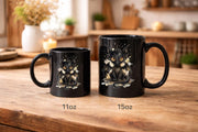 Black ceramic 11oz & 15oz mug featuring cute watercolor dragon with glowing eyes, styled on rustic wood table with candle, coffee beans, and cozy kitchen background