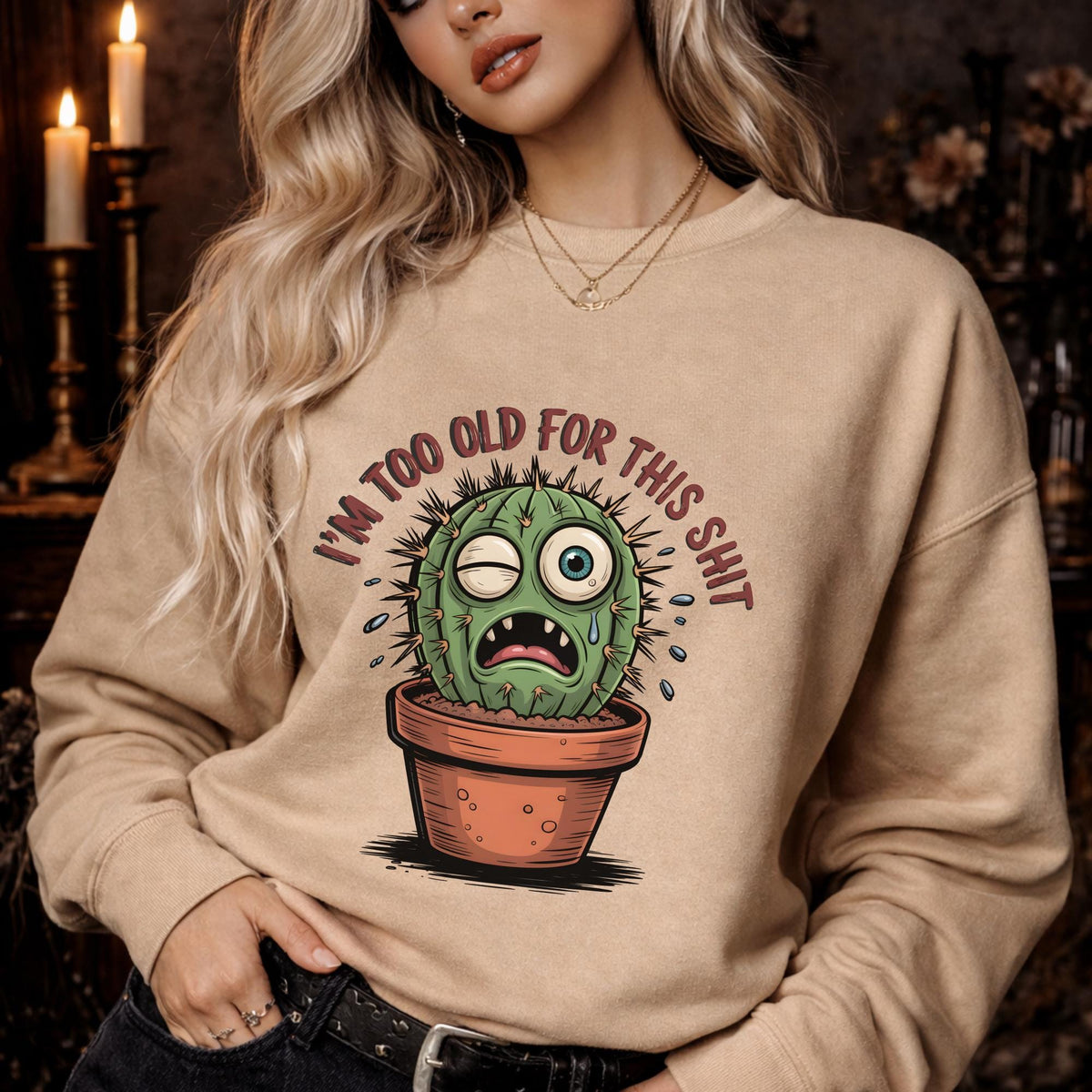 Woman wearing a sand Gildan 18000 sweatshirt featuring a funny cactus graphic with the phrase “I’m too old for this shit,” styled casually in a cozy, warm-toned aesthetic setting.