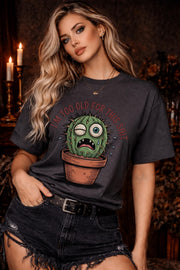 Woman wearing a Gildan 5000 t-shirt featuring a funny cactus graphic with the phrase “I’m too old for this shit,” styled with black distressed shorts in a warm, dark aesthetic setting.