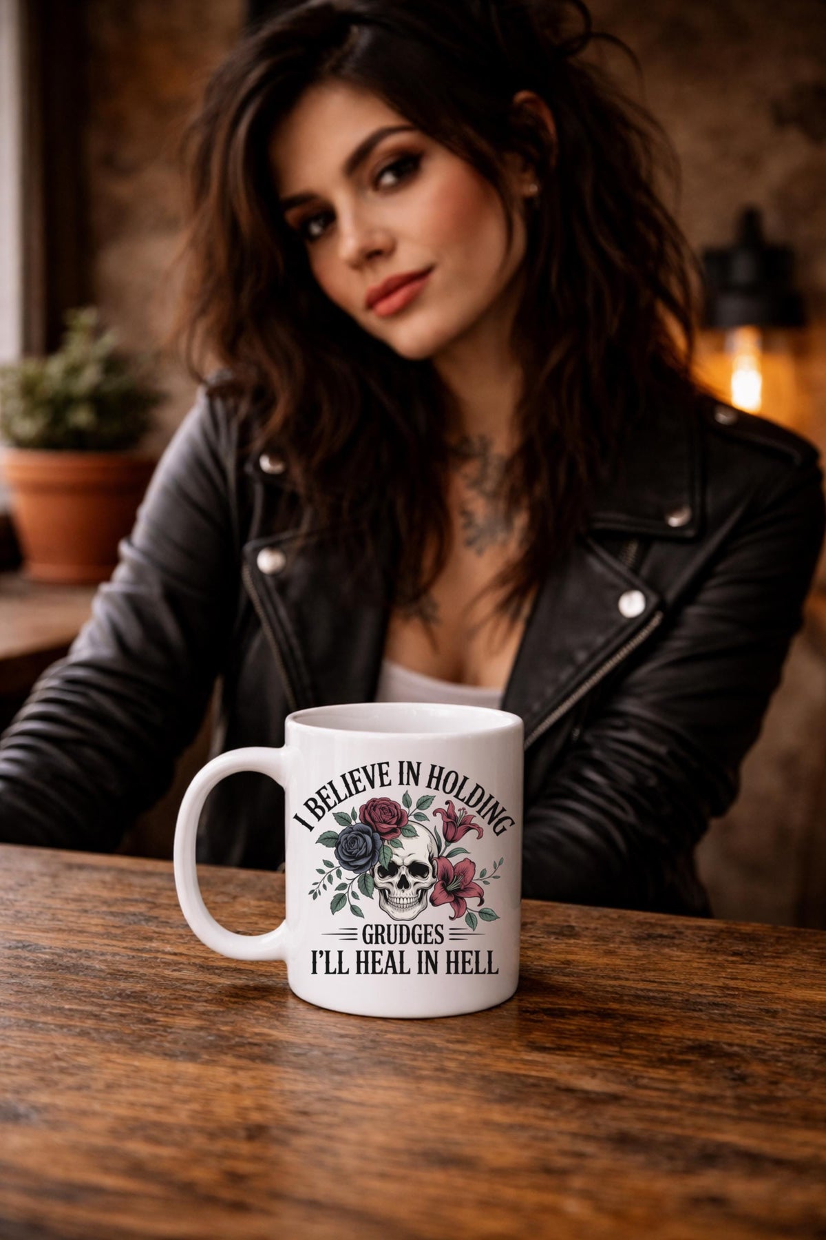 A women sitting at a cafe with her mug on the table, I Believe in Holding Grudges Mug – Skull Floral Gothic Coffee Cup – Dark Humor Gift – 11oz 15oz Ceramic Mug