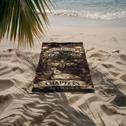 Dark gothic beach towel with death before chapters design featuring skulls moth and books laid on sandy beach near ocean