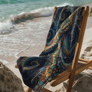 Octopus beach towel with colorful swirl pattern draped over wooden chair on sandy beach by ocean waves