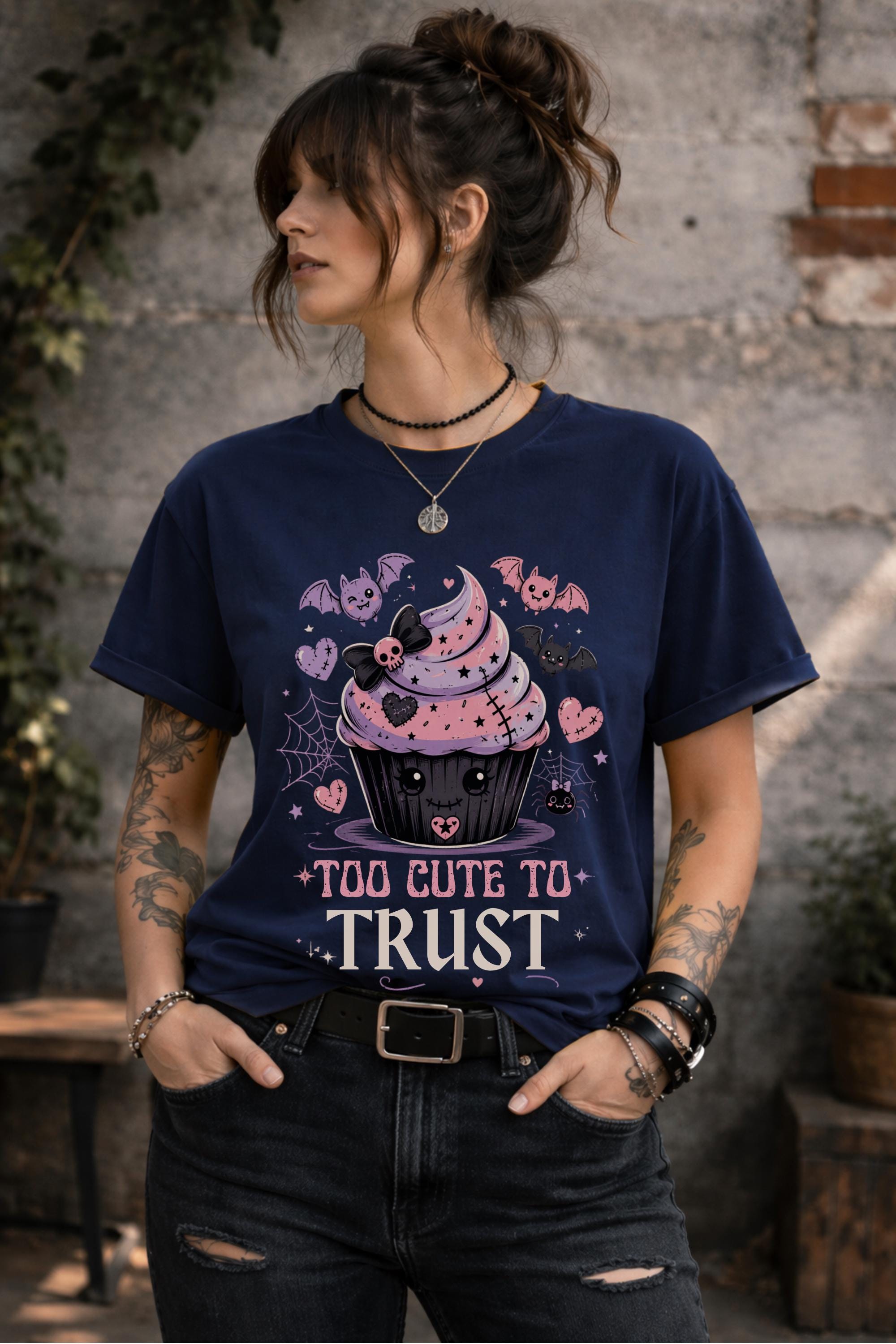 Woman wearing a graphic t-shirt featuring spooky kawaii cupcake with bats hearts spiderwebs and Too Cute to Trust quote
