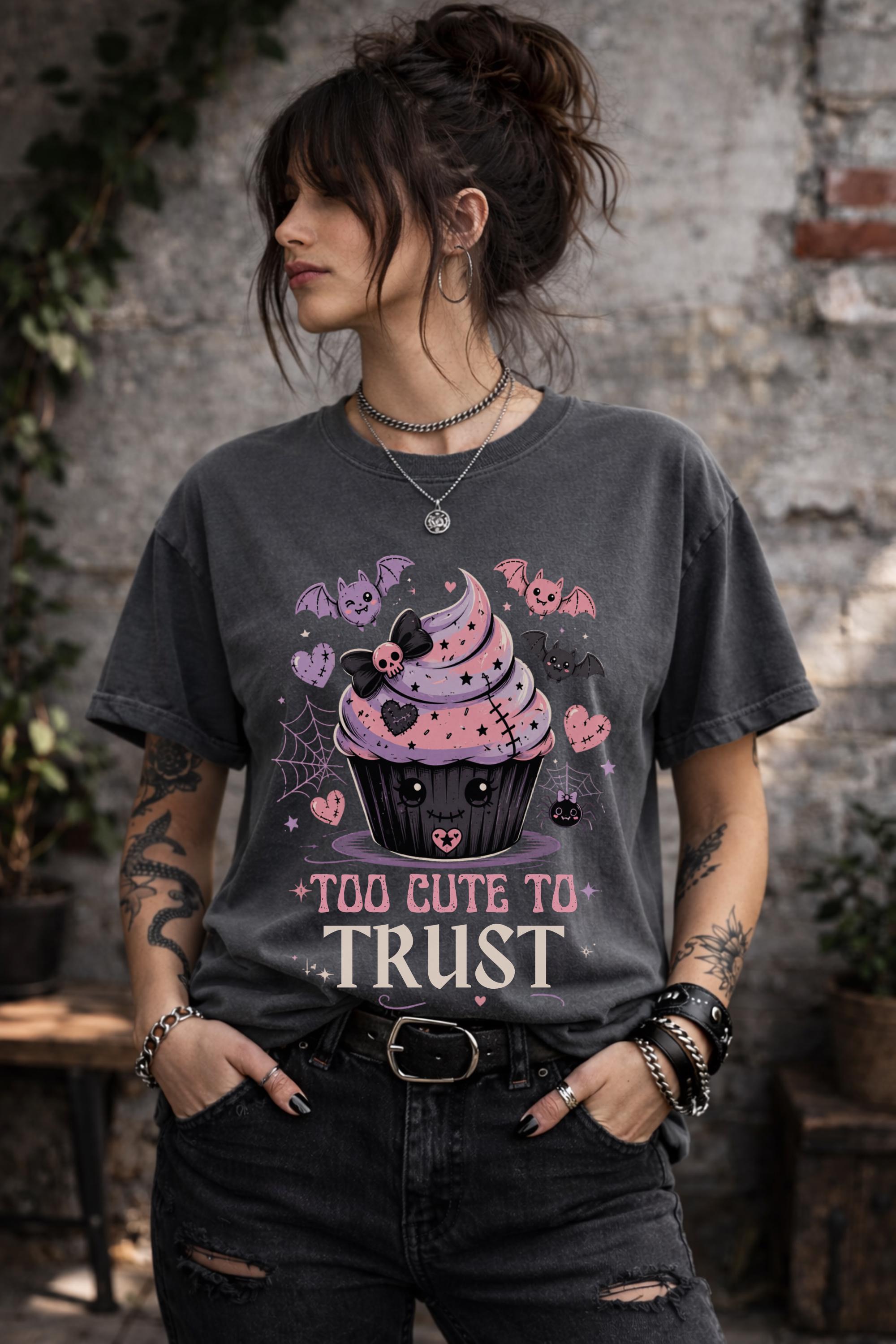 Woman wearing a graphic t-shirt featuring spooky kawaii cupcake with bats hearts spiderwebs and Too Cute to Trust quote